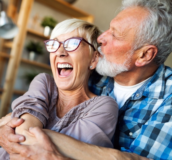 Older couple laughing together after dental implant tooth replacement