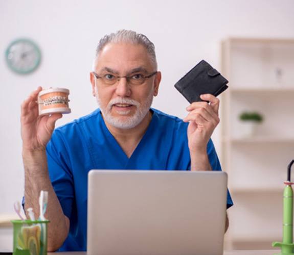 A dentist holding up a jaw mockup and a wallet 