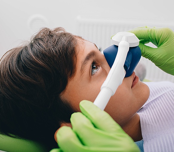 Dentist placing nitrous oxide sedation dentistry mask on young patient