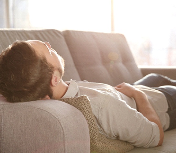 Man resting on couch after tooth extraction in Marion