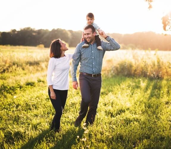 Family of three smiling outdoors after family dentistry