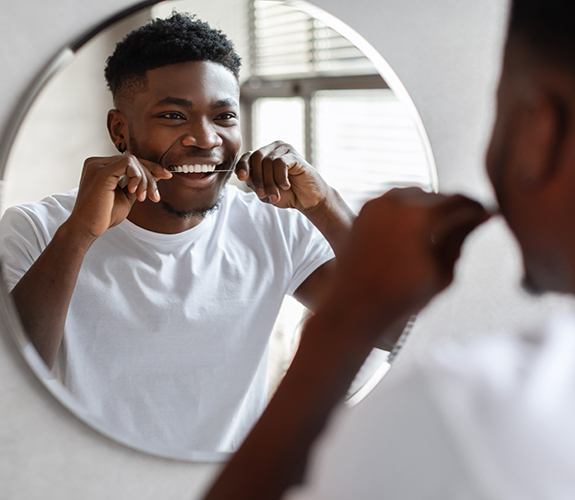 Man smiling while flossing his teeth in bathroom