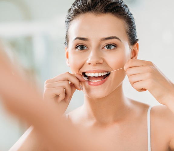 Woman flossing teeth to care for porcelain veneers