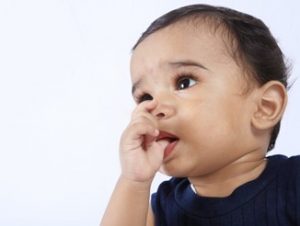 A toddler wearing a navy-blue shirt is sucking his thumb