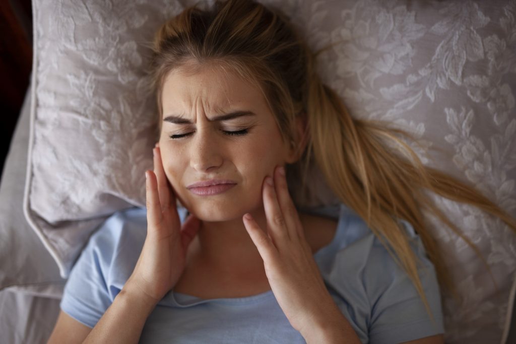 Woman experiencing jaw pain from teeth grinding while sleeping