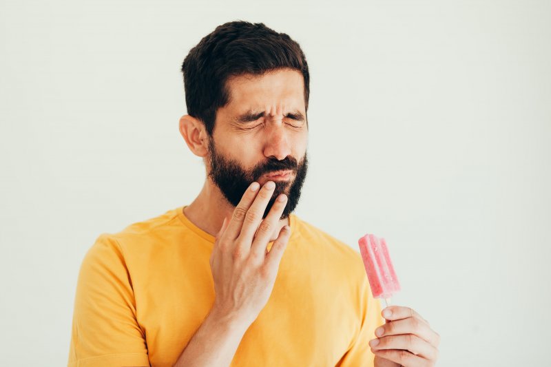 Person holding an ice cream cone and holding their cheek in pain